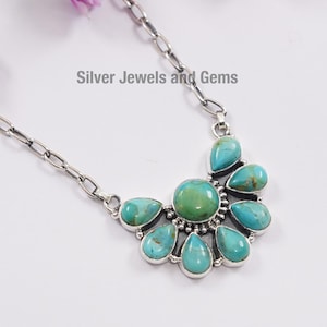 May include: A silver necklace with a turquoise pendant. The pendant features a large, round turquoise stone surrounded by smaller turquoise stones. The necklace has a chain link design. The text "Silver Jewels and Gems" is visible.