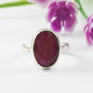 Op de afbeelding: Een zilveren ring met een dieprode ovale edelsteen in een bezel-setting.