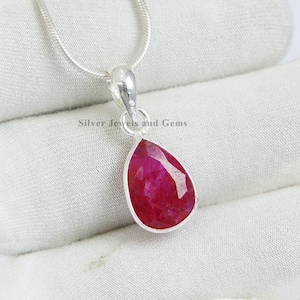 Op de afbeelding: Een zilveren ketting met een traanvormige hanger met een rode robijn.