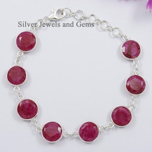 Op de afbeelding: Een zilveren armband met een kettingontwerp en acht ronde rode robijn edelstenen. De armband heeft een kreeftensluiting.