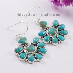 May include: A pair of silver earrings with turquoise stones. The earrings are shaped like a flower with a central round stone surrounded by smaller stones.