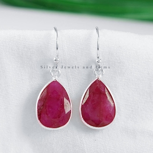 Può includere: Un paio di orecchini pendenti in argento con pietre preziose di rubino rosso a forma di goccia. Gli orecchini hanno un design semplice e sono perfetti per l'uso quotidiano.