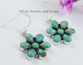 May include: A pair of silver earrings with turquoise flower-shaped pendants. Each earring features seven turquoise stones set in a silver flower design.