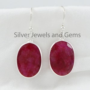 Könnte beinhalten: Ein Paar silberne Ohrringe mit ovalen roten Edelsteinen. Die Ohrringe haben ein schlichtes Design und sind perfekt für den Alltag.