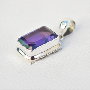 May include: A silver pendant featuring a large, rectangular, purple gemstone. The pendant has a simple, elegant design and is ideal for adding a touch of sparkle to any outfit.
