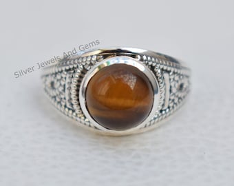 May include: A silver ring with a brown tiger's eye gemstone set in a bezel setting. The ring has a textured band with a geometric design.