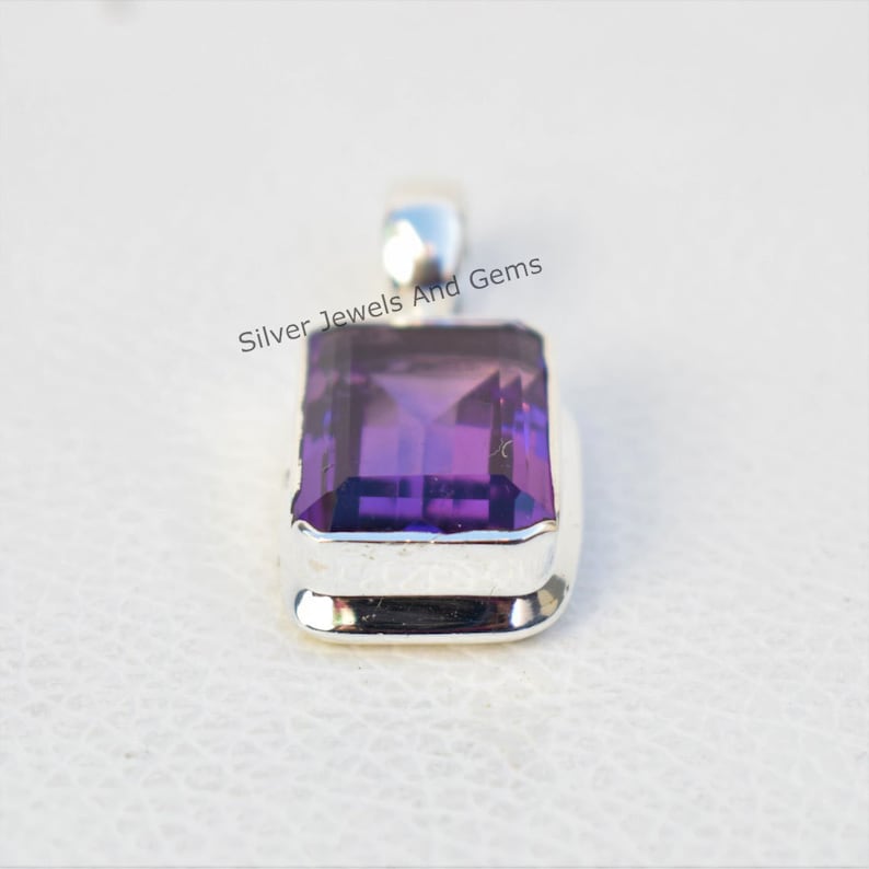 May include: A silver pendant featuring a large, rectangular, purple amethyst gemstone. The gemstone is set in a silver bezel with a smooth, polished finish. The pendant is a simple and elegant design.