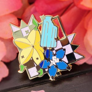 May include: A colorful enamel pin featuring a yellow starfruit, blue and white flowers, and a light blue pitcher. The pin has gold-colored outlines and a checkered pattern, with a pink glittery background.
