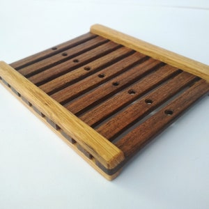 May include: A wooden soap dish with a slatted design. The dish is made of two types of wood, one light brown and one dark brown. The dish has several drainage holes.