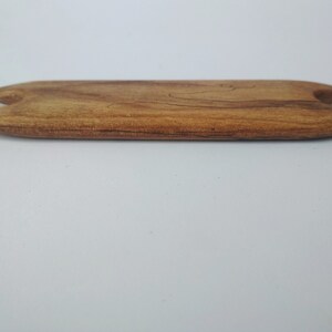 May include: A wooden tool with a rounded, slightly curved shape and two pointed ends. The tool is made of light brown wood with darker brown streaks.