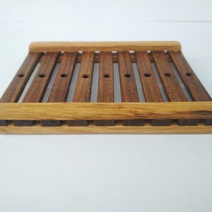 May include: A wooden soap dish with a slatted design. The dish is made of two different types of wood, one light brown and one dark brown.