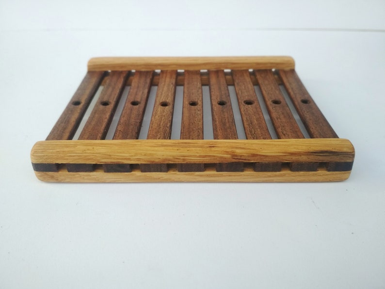 May include: A wooden soap dish with a slatted design. The dish is made of two different types of wood, one light brown and one dark brown.