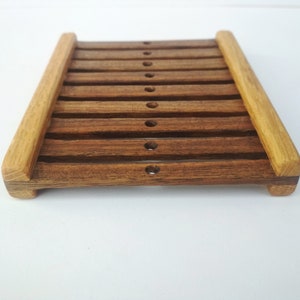 May include: A wooden soap dish with a slatted design. The dish is made of dark brown wood with lighter brown wood accents. The dish has a rectangular shape and is approximately 6 inches long and 4 inches wide.