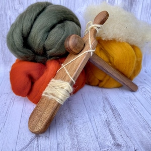 May include: A wooden hand spindle with three balls of wool in green, orange, and yellow. The spindle is made of wood and has a simple design.