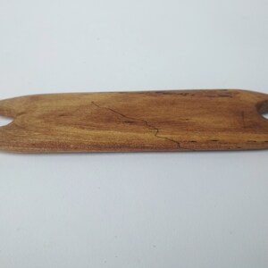 May include: A wooden tool with a cat-shaped design, made of light brown wood with dark brown grain patterns.