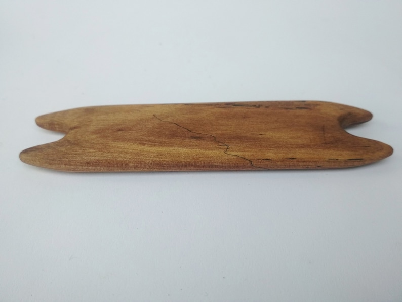 May include: A wooden tool with a cat-shaped design, made of light brown wood with dark brown grain patterns.
