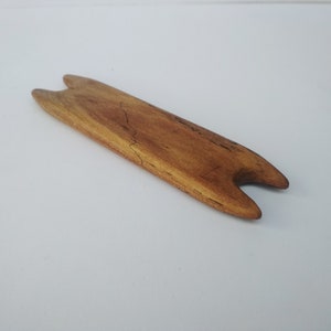 May include: A wooden knitting needle tool with two prongs at each end. The tool is light brown and has a natural wood grain.
