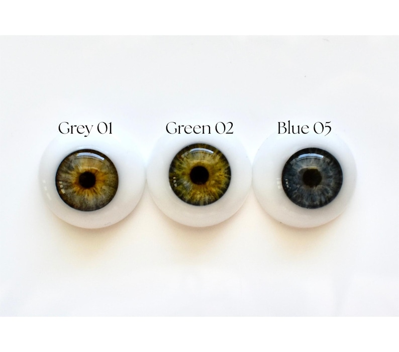 K&ouml;nnte beinhalten: Drei Puppenaugen mit unterschiedlich farbigen Iris, eingesetzt in wei&szlig;em Kunststoff. Die Iris sind grau, gr&uuml;n und blau. &Uuml;ber jedem Auge steht der Text "Grey 01", "Green 02" und "Blue 05".