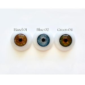 K&ouml;nnte beinhalten: Drei Puppenaugen mit wei&szlig;en Sklera werden gezeigt. Die Augen sind mit "Hazel 01", "Blue 02" und "Green 04" beschriftet. Das haselnussfarbene Auge hat eine braune Iris, das blaue Auge hat eine blaue Iris und das gr&uuml;ne Auge hat eine gr&uuml;ne Iris. Jedes Auge hat eine schwarze Pupille.