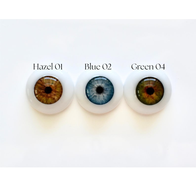 K&ouml;nnte beinhalten: Drei Puppenaugen mit wei&szlig;en Sklera werden gezeigt. Die Augen sind mit "Hazel 01", "Blue 02" und "Green 04" beschriftet. Das haselnussfarbene Auge hat eine braune Iris, das blaue Auge hat eine blaue Iris und das gr&uuml;ne Auge hat eine gr&uuml;ne Iris. Jedes Auge hat eine schwarze Pupille.
