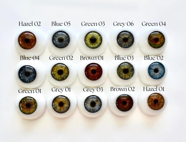 K&ouml;nnte beinhalten: Eine Sammlung von f&uuml;nfzehn Puppenaugen in verschiedenen Farben, darunter Hazel, Blau, Gr&uuml;n und Grau. Jedes Auge ist in einer wei&szlig;en, abgerundeten Basis eingesetzt, mit der Farbe und Nummer jedes Auges dar&uuml;ber gedruckt.
