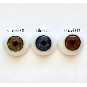 K&ouml;nnte beinhalten: Drei Puppenaugen mit wei&szlig;em Hintergrund. Die Augen sind mit "Green 01", "Blue 04" und "Hazel 02" beschriftet. Das gr&uuml;ne Auge hat eine braune und gr&uuml;ne Iris, das blaue Auge hat eine dunkelblaue Iris und das haselnussfarbene Auge hat eine braune Iris.