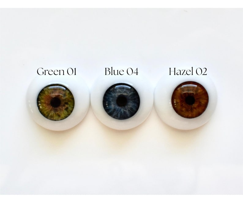 K&ouml;nnte beinhalten: Drei Puppenaugen mit wei&szlig;em Hintergrund. Die Augen sind mit "Green 01", "Blue 04" und "Hazel 02" beschriftet. Das gr&uuml;ne Auge hat eine braune und gr&uuml;ne Iris, das blaue Auge hat eine dunkelblaue Iris und das haselnussfarbene Auge hat eine braune Iris.