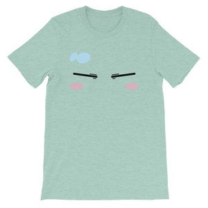 May include: A light green t-shirt with a cartoon face printed on the front. The face has black eyebrows, pink cheeks, and a light blue dot on the forehead.