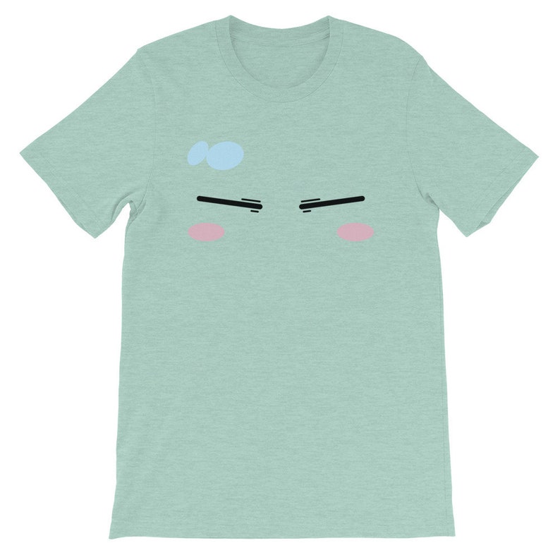May include: A light green t-shirt with a cartoon face printed on the front. The face has black eyebrows, pink cheeks, and a light blue dot on the forehead.
