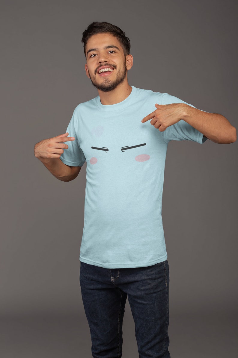 May include: A light blue t-shirt with a cartoon face printed on the front. The face has black eyebrows, pink cheeks, and a neutral expression.