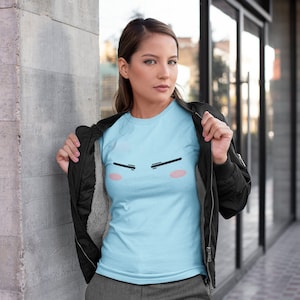 May include: A light blue t-shirt with a cartoon face graphic. The face has black eyebrows, pink cheeks, and a black mouth.