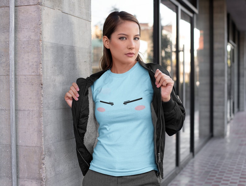 May include: A light blue t-shirt with a cartoon face graphic. The face has black eyebrows, pink cheeks, and a black mouth.