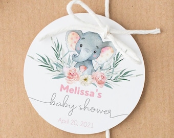 Op de afbeelding: Een ronde, witte baby shower-favorietentag met een aquarel-illustratie van een grijze olifant met roze accenten, omringd door roze bloemen en groene bladeren. De tekst op de tag luidt "Melissa's baby shower April 20, 2021".
