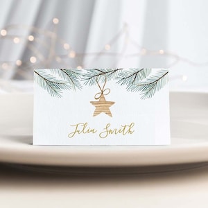 Peut inclure: Une carte de table blanche avec un motif de branche de pin verte et une étoile dorée. Le nom "Julin Smith" est écrit en lettres dorées.