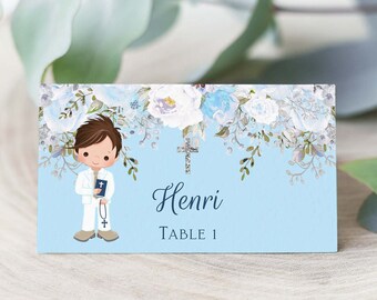 May include: Blue and white floral place card with a cartoon illustration of a boy in a white suit holding a book and rosary beads. The text on the card reads "Henri Table 1".