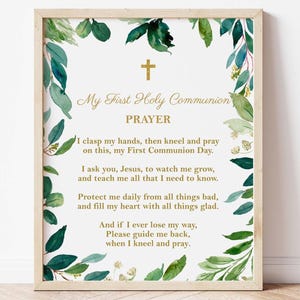 May include: A framed print with the text "My First Holy Communion Prayer" in gold script, featuring a gold cross and watercolor greenery. The prayer text is centered on a white background.