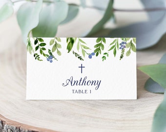 May include: White place card with a watercolor design of green leaves and blue berries. The card has a small cross and the text "Anthony Table 1".
