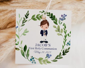 Puede incluir: Una tarjeta blanca con una ilustración de acuarela de un niño con traje sosteniendo un libro. La tarjeta tiene una corona de flores verdes con flores azules alrededor del niño. El texto en la tarjeta dice "Jacob's First Holy Communion May 20, 2023".