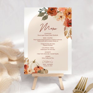 May include: A printable menu for a baby shower with a fall theme. The menu features a watercolor illustration of pumpkins and flowers in shades of orange, red, and brown. The text on the menu includes the words "Menu", "Startes", "Main Course", "Children's Menu", "Dessert", "Drinks", "Victoria's Baby Shower", and "October 24, 2023".