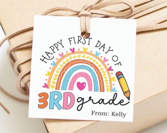 Könnte beinhalten: Ein weißes Geschenkanhänger mit einem Regenbogen und dem Text "Happy First Day of 3rd Grade" mit einem Bleistift und Herzen. Der Anhänger ist mit einem braunen Band an einer braunen Geschenkbox gebunden. Der Text "From: Kelly" befindet sich am unteren Rand des Anhängers.