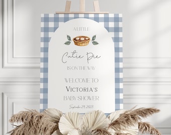Può includere: Un cartello di benvenuto per un baby shower blu e bianco a quadri con il testo "A Little Cutie Pie is on the way. Welcome to Victoria's Baby Shower. September 29, 2023". Il cartello presenta un'illustrazione ad acquerello di una torta.