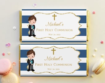 Puede incluir: Dos envoltorios de barra de chocolate a rayas azules y blancas con un borde dorado. Cada envoltorio presenta un niño de dibujos animados con traje sosteniendo un libro y una cruz. El texto en los envoltorios dice "Michael's First Holy Communion" y la fecha "May 20, 2022".