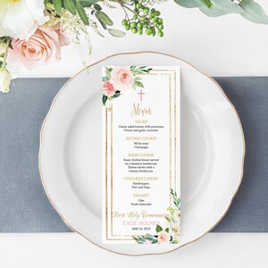 May include: A gold and white menu card with floral designs and a gold cross. The menu includes a salad, second course, main course, children's menu, and dessert. The text reads "Menu", "First Holy Communion", "Catie Holmes", and "May 20, 2019".
