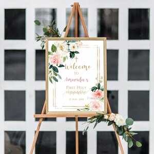 May include: Welcome to Amanda's First Holy Communion sign with a gold frame and floral design. The sign features a white background with pink and white flowers and greenery. The text is in gold and pink. The date is May 15, 2019.