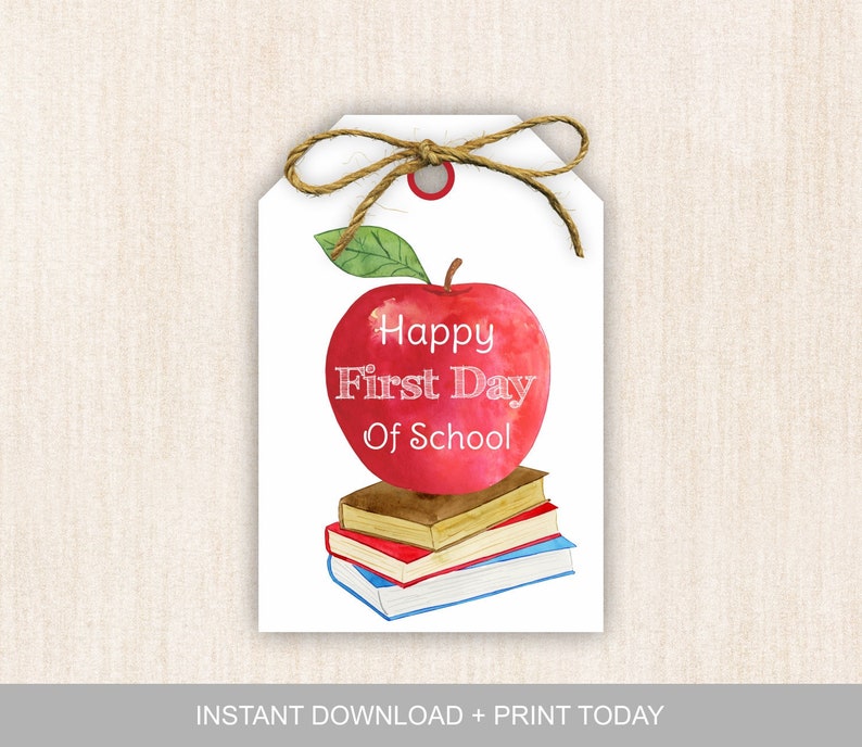 May include: A printable gift tag featuring a red apple with a green leaf on top of a stack of books. The apple has the text "Happy First Day Of School" on it.