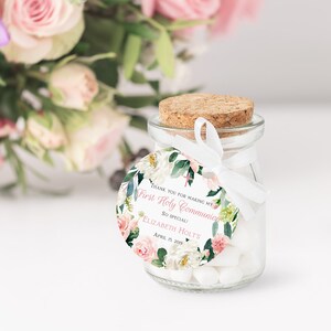 Pode incluir: Um pequeno frasco de vidro com tampa de corti&ccedil;a cheio de doces brancos. Uma etiqueta redonda branca com desenhos florais rosa e verdes est&aacute; presa ao frasco com uma fita branca. A etiqueta diz "Obrigado por tornar a minha Primeira Comunh&atilde;o t&atilde;o especial! Elizabeth Holt's Abril 15, 2019".
