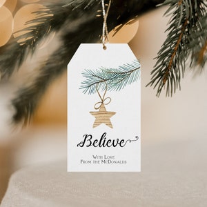 May include: A white gift tag with a watercolor illustration of a pine branch with a star ornament hanging from it. The text "Believe" is written in cursive with the words "With Love From the McDonalds" below.