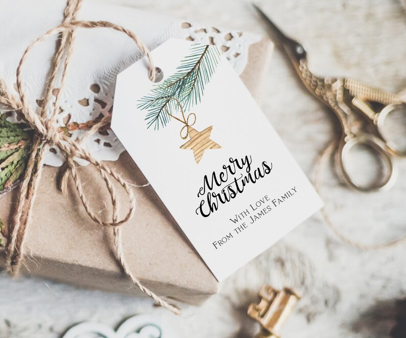 May include: A white gift tag with a watercolor illustration of a pine branch with a gold star ornament. The tag reads "Merry Christmas" with the text "With Love From The James Family" below.