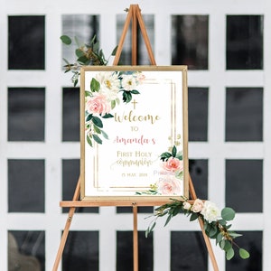 Pode incluir: Bem-vindo &agrave; Primeira Comunh&atilde;o de Amanda, sinal com moldura dourada e design floral. O sinal est&aacute; em um cavalete de madeira e tem um fundo branco com flores rosa e brancas. A data &eacute; 15 de maio de 2019.