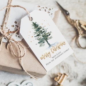 May include: A white gift tag with a watercolor illustration of a green pine tree with gold glitter. The text "merry christmas" is written in gold script with the words "with love from the Johnson's family" below.